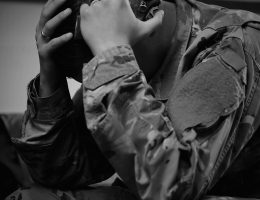 This is a black and white image of a soldier in full uniform holding a gun near his head.